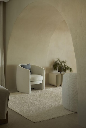 Relax in a spacious room with a high ceiling, plush armchair, and cozy rug.