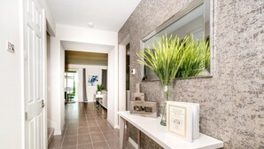 Un pasillo con un mostrador de recepción blanco, un certificado enmarcado y un espejo que refleja una planta.