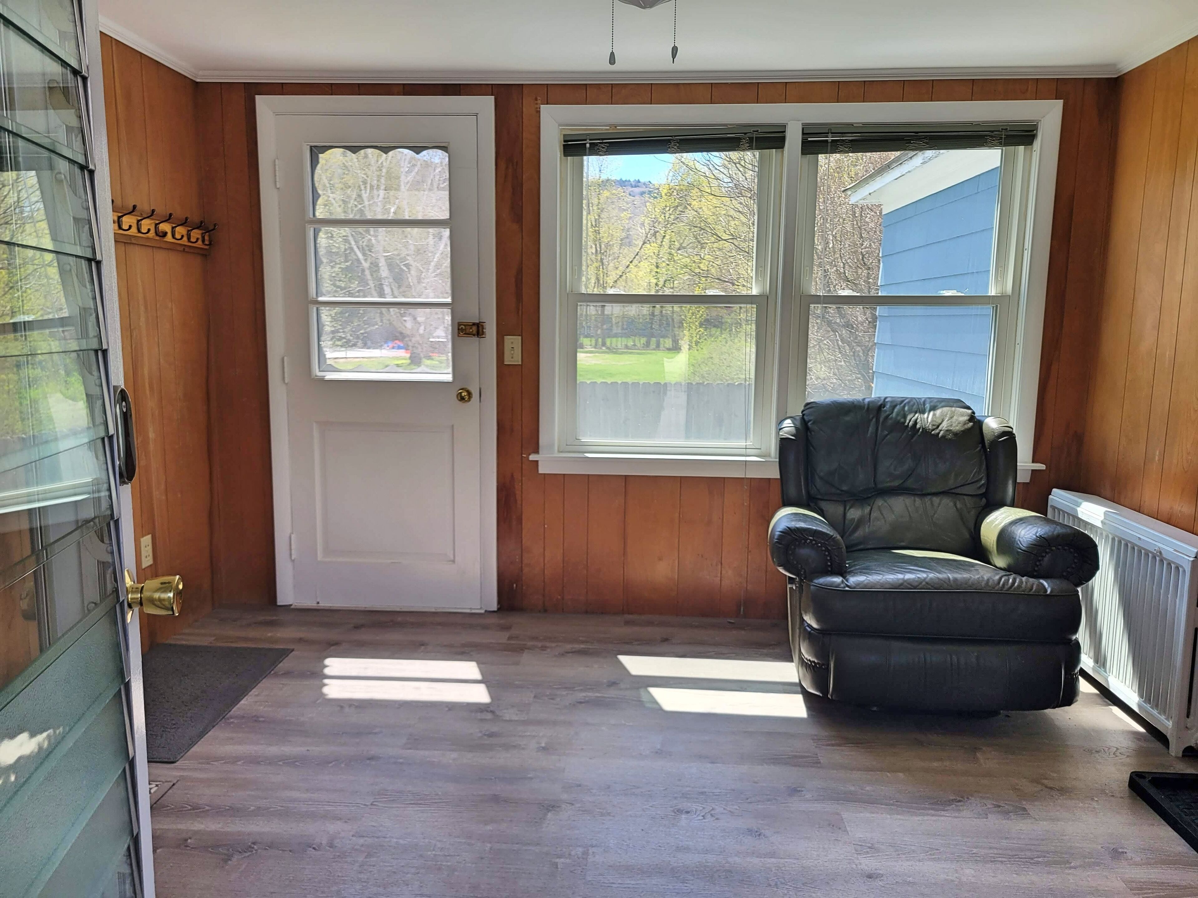 A room with a wooden door, a black leather chair, and a large window with a view of a house and trees.