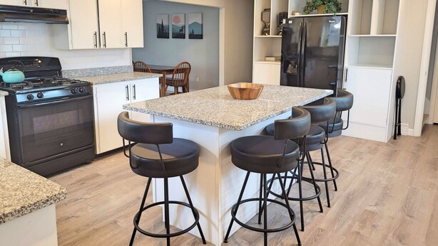 A modern kitchen with a central island, bar stools, a stove, and a refrigerator.