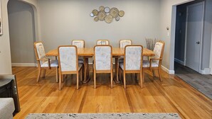 A dining area with a wooden table and six chairs, a decorative wall piece, and a door to the right.
