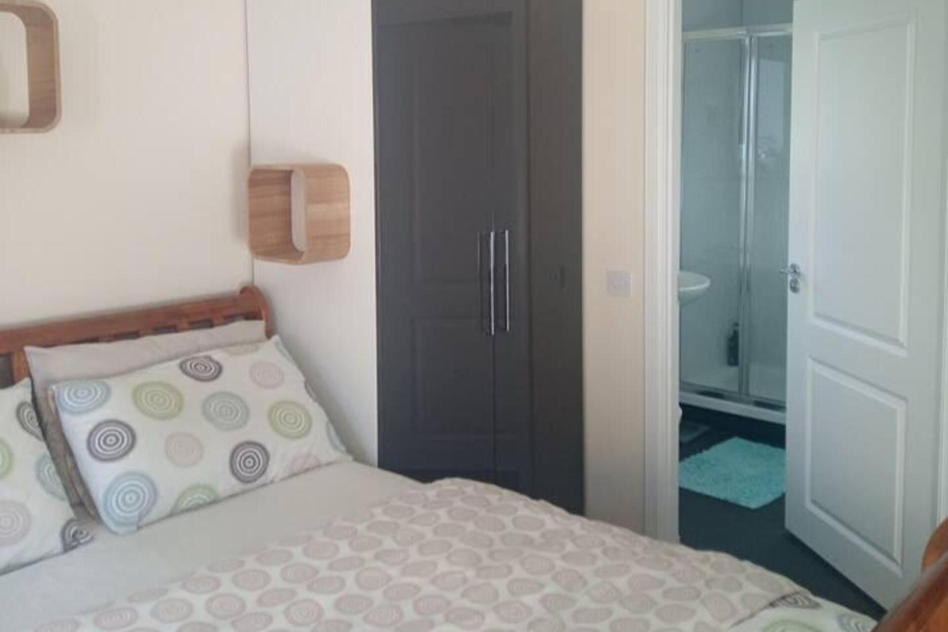 Une chambre à coucher avec un lit, une porte sombre et un espace douche visible à travers une porte ouverte.