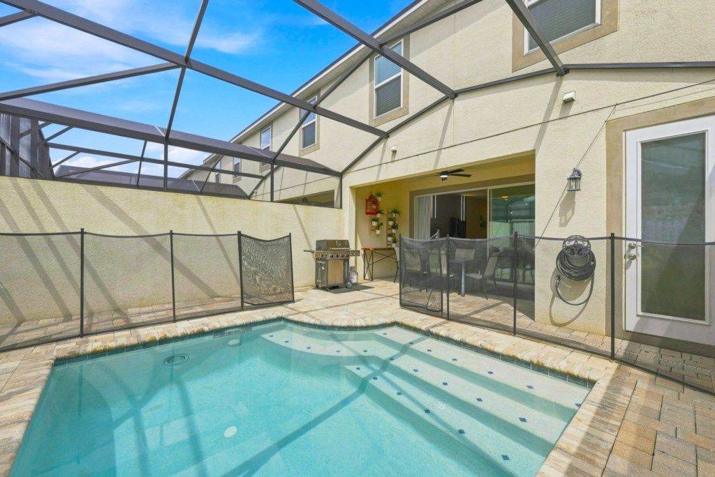 Ein Schwimmbad mit Glasveranda, ein Grill und eine überdachte Terrasse.