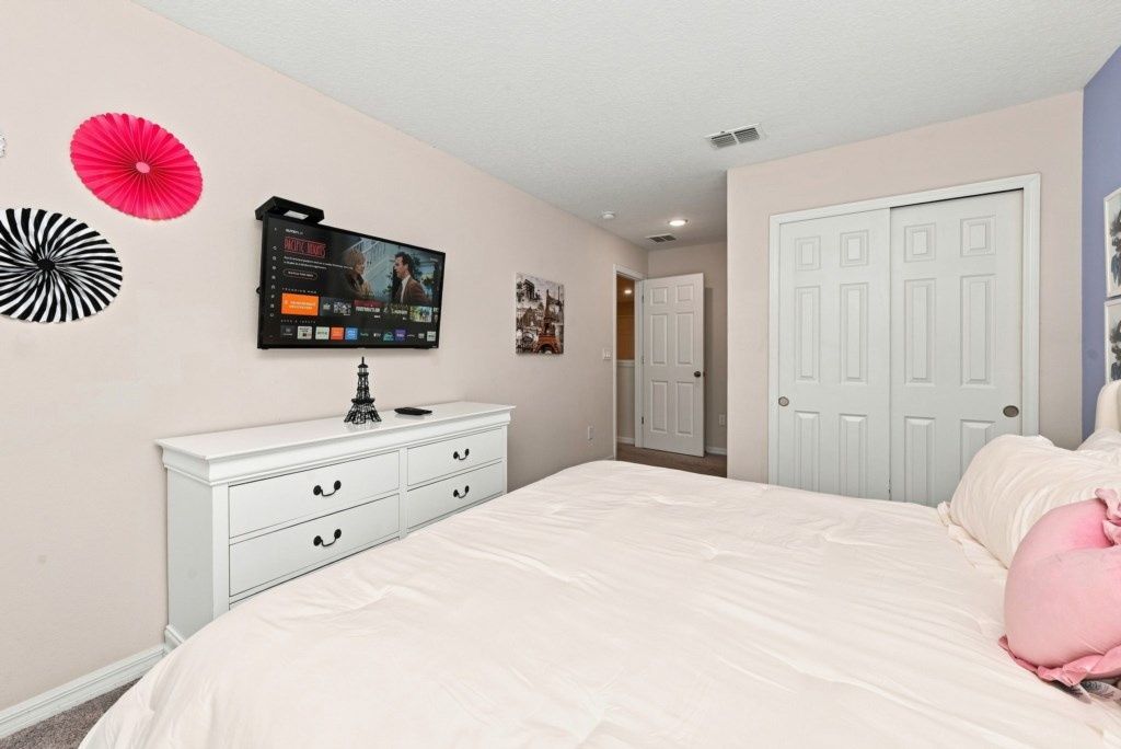 Un dormitorio con una cama, un aparador, un televisor y una puerta.