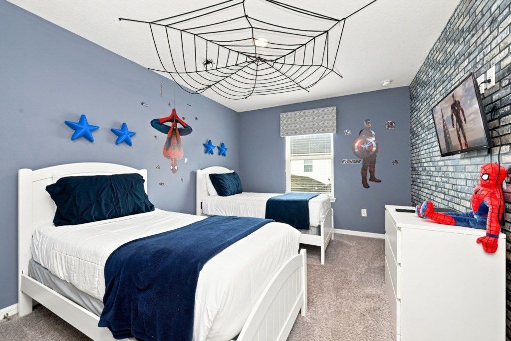 A bedroom with two beds, a spider web ceiling design, and a Spider-Man plush toy.