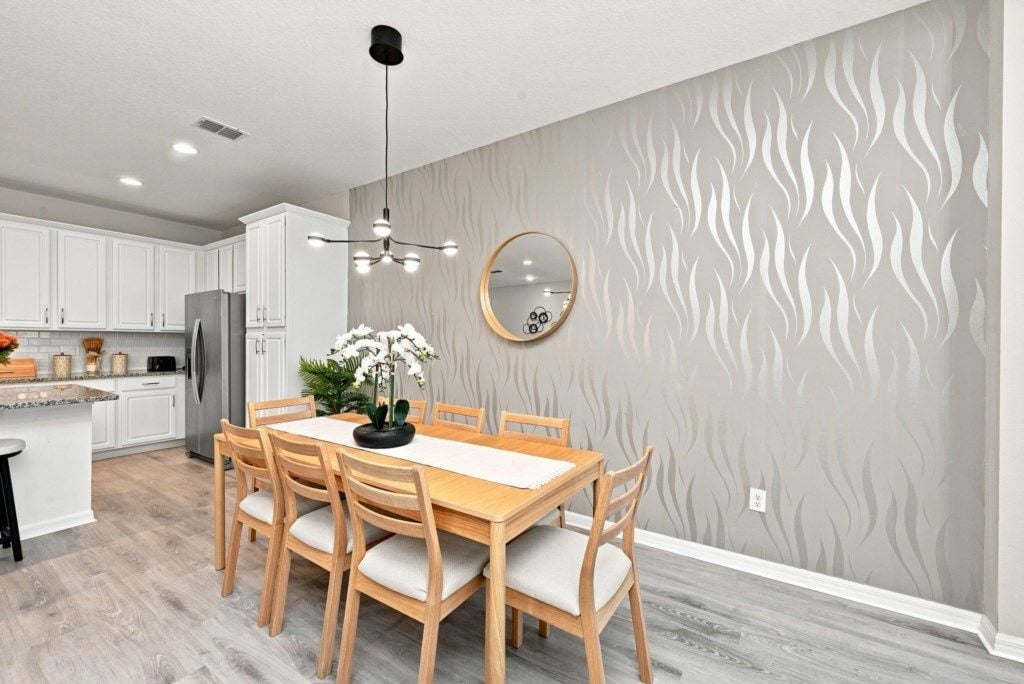 A modern kitchen with white cabinetry, a wooden dining table, and a patterned wall.