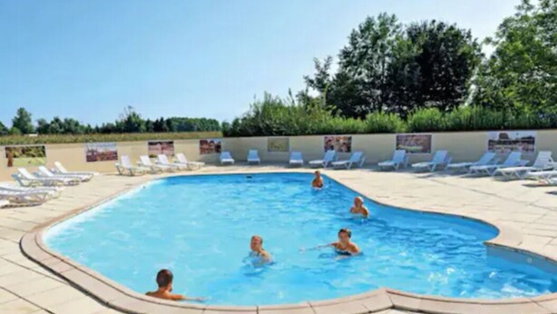 Una piscina con sillas de descanso y gente nadando.
