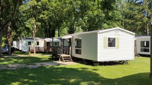 Una hilera de viviendas móviles en un camping, con zonas verdes y árboles al fondo.