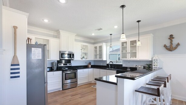 A modern kitchen with white cabinets, stainless steel appliances, and a wooden island with bar stools. - Everleigh After 3 Bedroom Home by RedAwning (Port Bolivar)