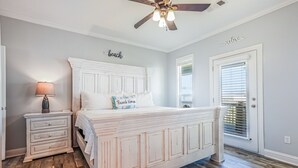A bedroom with a white bed, a nightstand, a ceiling fan, and a door with a window. - Everleigh After 3 Bedroom Home by RedAwning (Port Bolivar)