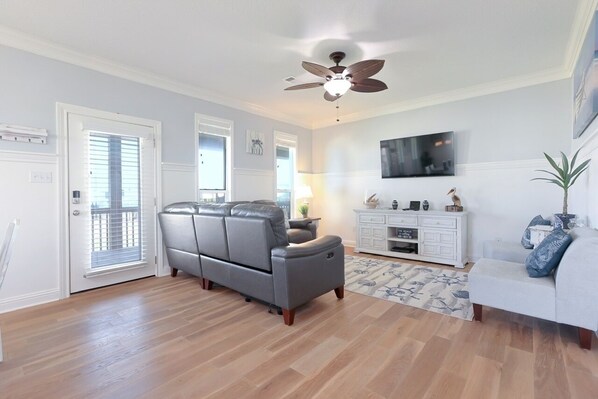 A spacious living room with a gray leather sofa, a white entertainment unit, and a ceiling fan.
