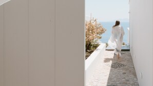 A narrow stone pathway leading to a white building with a view of the sea.