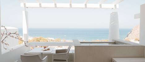 A balcony with a view of the sea, white furniture, and a pergola structure.