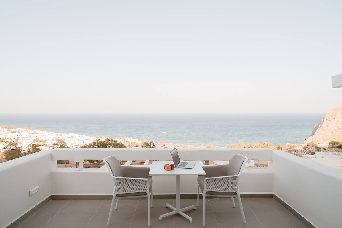 Un balcón con una mesa blanca y dos sillas, con vista al mar.