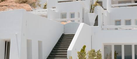 Een modern wit gebouw met een zwembad, terras en een trap naar een balkon.