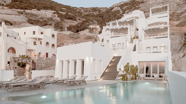 A modern resort with a pool, white buildings, and a mountainous backdrop.