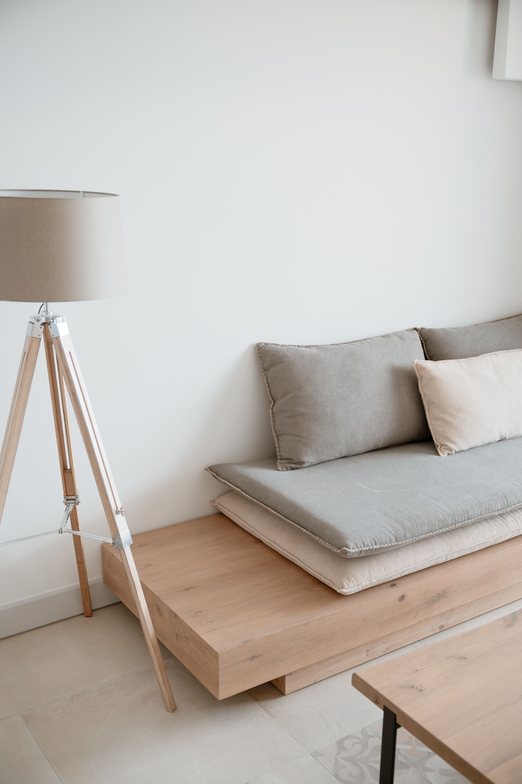 Una habitación minimalista con suelo de madera, un sofá gris con cojines, una mesa de centro de madera y una lámpara de pie.