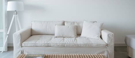 Una sala de estar moderna con un sofá color beige, una mesa de centro tejida y una lámpara de pie.