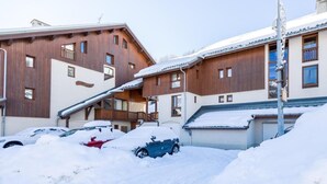 A building with a wooden facade, multiple windows, and a covered parking area with snow. - 150m from ski slopes, Ground floor, terrace, parking, tv, 27m², Valloire (Valloire)