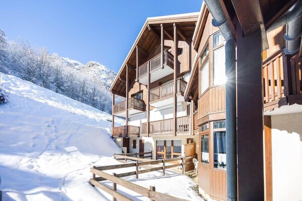 Eine Holzhütte mit Balkonen, einem Holzzaun und einem verschneiten Berg im Hintergrund.