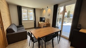 A dining area with a wooden table and chairs, a sofa, and a television. - 350m from ski slopes, 2nd floor, sauna, terrace, ski locker, 41m², Valloire (Valloire)