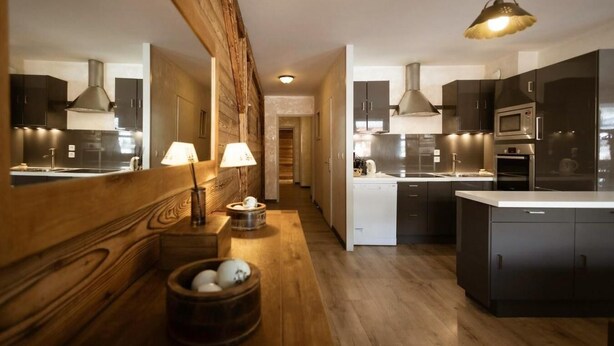 Une cuisine moderne avec des meubles de couleur sombre, des appareils en acier inoxydable et des éléments décoratifs en bois.