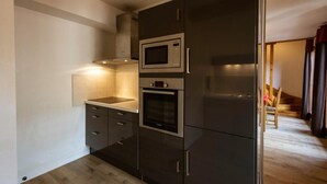 A compact kitchen with a microwave, oven, and refrigerator, featuring dark cabinetry and a light countertop.