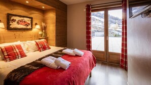 A hotel room with a wooden headboard, a bed with red and white bedding, a red and white checkered curtain, and a view of a snowy landscape through a sliding door.
