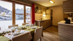 A dining area with a table set for four, a kitchen with modern appliances, and a view of a snowy landscape through large windows.