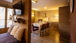 Una camera accogliente con interni in legno, una TV fissata al muro, un'area pranzo con tavolo e sedie e una cucina con pensili in legno.