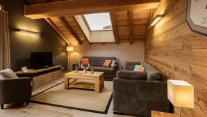 Una sala de estar estilo loft acogedora, con techo inclinado, paredes de madera, televisor de pantalla plana, un conjunto de sofás y una mesa de centro.