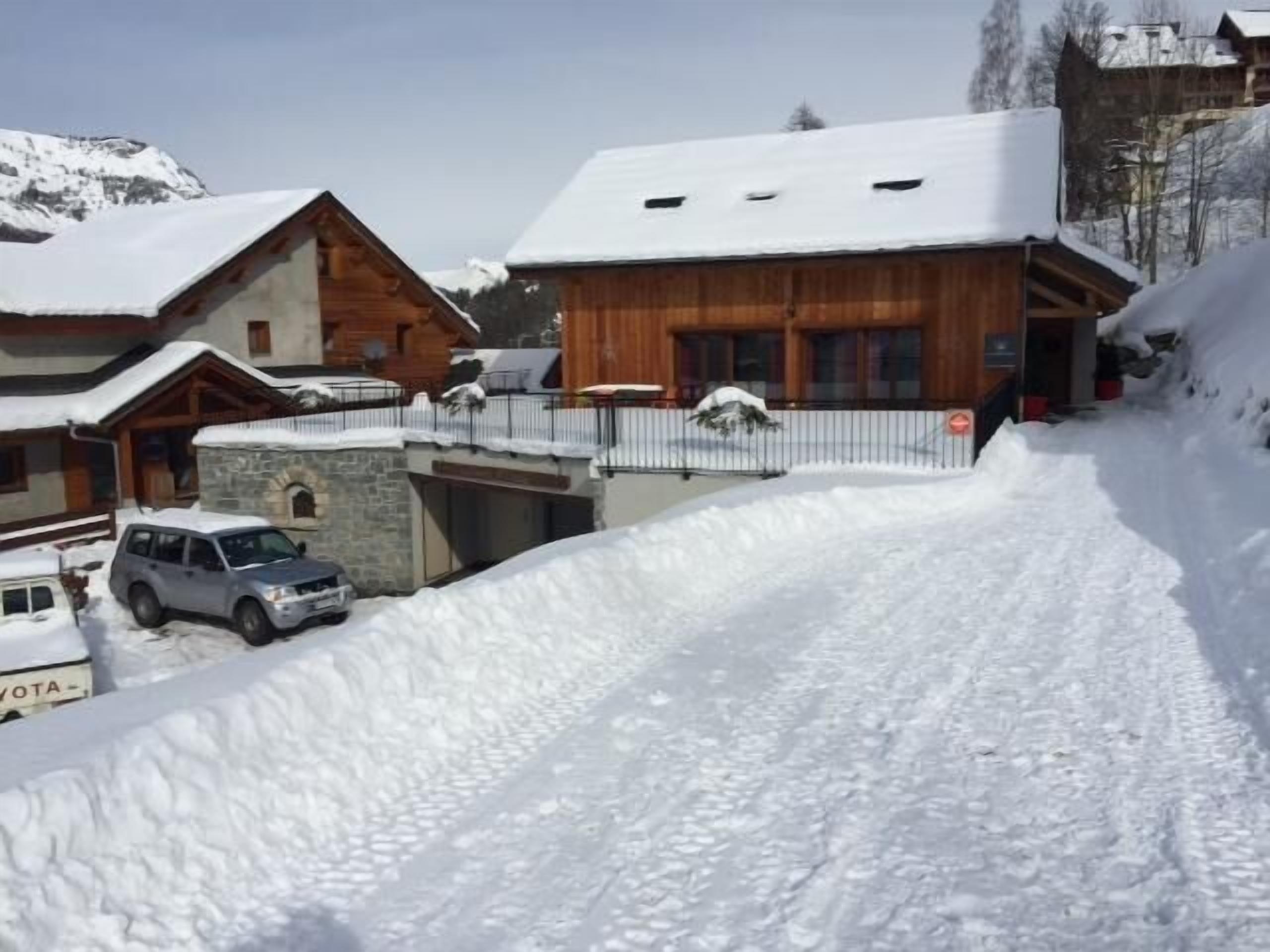 Un chalet de montagne enneigé, doté d’une entrée en pierre, d’une façade en bois et d’une allée pavée.