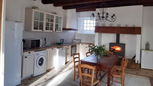 A kitchen with a wooden table, chairs, a washing machine, a microwave, and a fireplace.