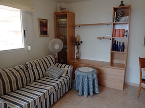 Uma sala de estar com um sofá listrado, uma pequena mesa redonda, um armário com portas de vidro e uma estante.