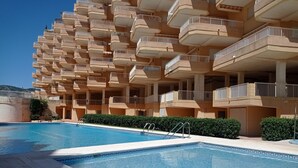 A hotel with a pool, multiple balconies, and a clear sky.