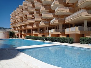A hotel with a pool, multiple balconies, and a clear sky.