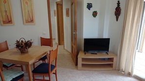 A dining area with a wooden table, chairs, a television on a stand, and wall decorations.