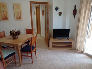 A dining area with a wooden table, chairs, a television on a stand, and wall decorations.