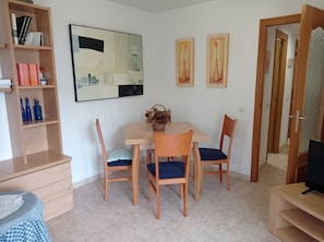 Uma área de refeições com mesa, cadeiras, estante e televisão.