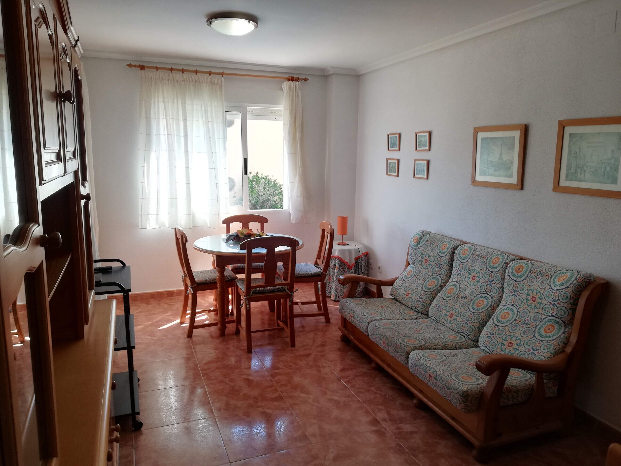 Een woonkamer met een bank, een eettafel, stoelen en een raam met gordijnen.