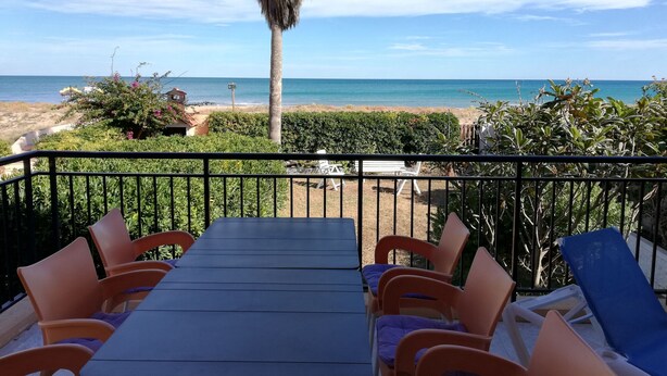 A balcony with a table and chairs, overlooking a beach and the ocean.