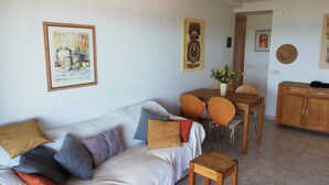 A living room with a sofa, a small wooden table, a dining table with chairs, and a cabinet.