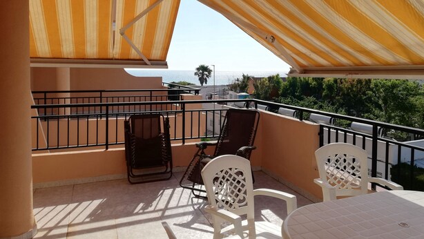 Ein Balkon mit Meerblick, ausgestattet mit Streifenmarkisen, einem Tisch und zwei Stühlen.