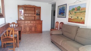 Ein Wohnzimmer mit einer Couch, einem Holzesstzimmer, Stühlen und einer Küchenzeile mit Schränken und einer Arbeitsfläche.
