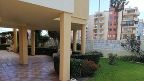 Un espacio al aire libre techado con piso de baldosas, césped y cerca blanca.