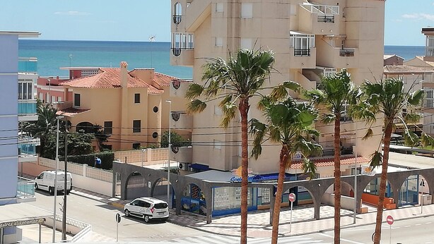 Un edificio de varios pisos con balcones, un paseo peatonal y palmeras.