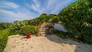 A gravel pathway leading to a stone staircase surrounded by lush greenery and potted plants. - Appartamento Villa da 4 Fino a 5 Persone Giardino (Capoliveri)