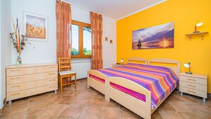 A bedroom with a bed, a chair, a desk, a radiator, a window with curtains, a painting on the wall, and a lamp on the bedside table. - Appartamento Villa da 4 Fino a 5 Persone Giardino (Capoliveri)
