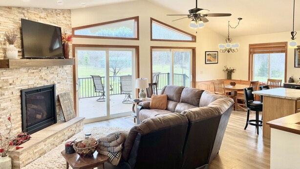 A spacious living room with a fireplace, a television, a large sofa, and a dining area with a kitchen in the background. - Cheerful cottage w/ fireplace. Great location for exploring the Lake Pepin area! (Pepin)