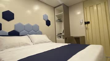 Quarto de hotel com uma cama grande, um guarda-roupa, uma escrivaninha e um espelho.